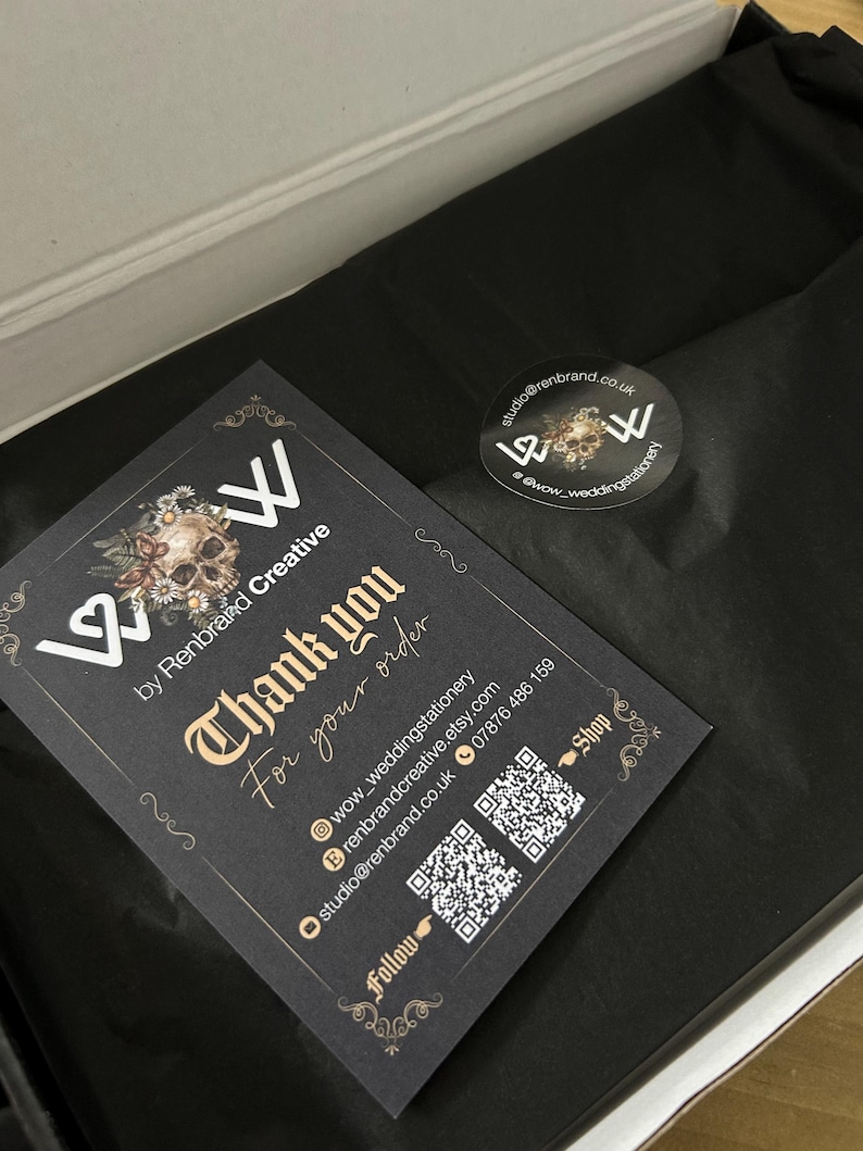 May include: A black card with gold text that reads "Thank you for your order" is placed inside a box with black tissue paper. A sticker with a skull design and the text "wow_weddingstationery" is also visible.