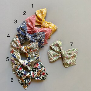 Puede incluir: Siete lazos para el pelo con estampado floral en varios colores y patrones. Los lazos est&aacute;n dispuestos en semic&iacute;rculo sobre un fondo gris.