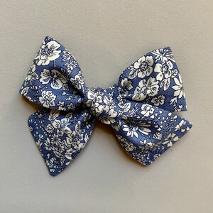 Puede incluir: Un lazo para el pelo de color azul y blanco con estampado floral. El lazo est&aacute; atado en un nudo y tiene una forma puntiaguda.
