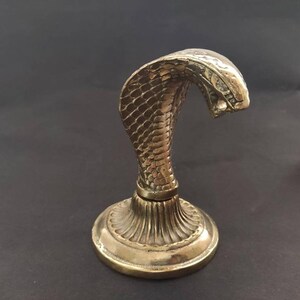 Brass hooded snake figurine with arched neck on a ribbed pedestal, ideal for desk or office decor.