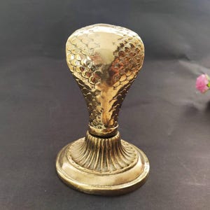 Brass hooded snake figurine with arched neck on a ribbed pedestal, ideal for desk or office decor.