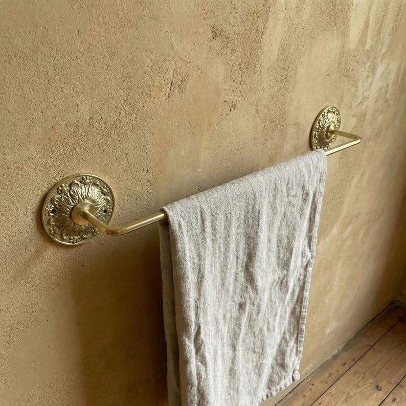 Handmade brass towel bar wall mounted in bathroom holding white towel