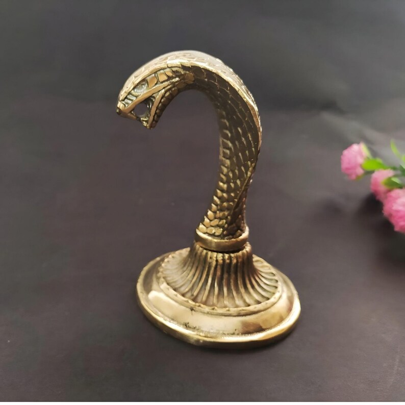 Brass hooded snake figurine with arched neck on a ribbed pedestal, ideal for desk or office decor.