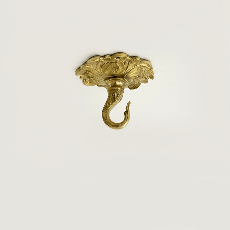 May include: Gold ceiling hook with a decorative floral design. The hook is designed to hold a chandelier or other heavy object.