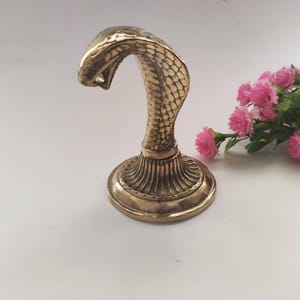Brass hooded snake figurine with arched neck on a ribbed pedestal, ideal for desk or office decor.