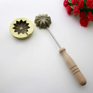 Può includere: Un set di due stampi a forma di fiore in ottone per fare biscotti o altri dolcetti. Gli stampi hanno la forma di una margherita con un design in rilievo. Uno stampo è attaccato a un manico in legno.