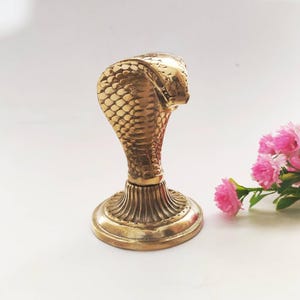 Brass hooded snake figurine with arched neck on a ribbed pedestal, ideal for desk or office decor.