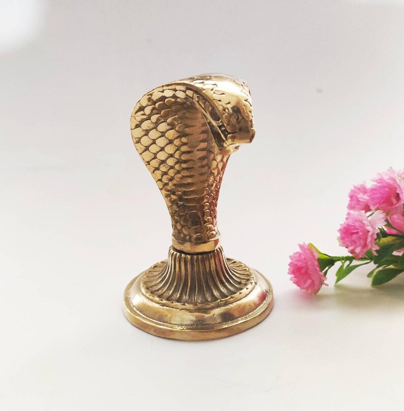 Brass hooded snake figurine with arched neck on a ribbed pedestal, ideal for desk or office decor.