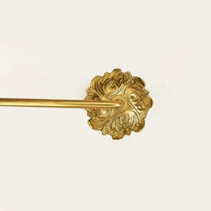 Op de afbeelding: Gouden metalen handdoekrek met een sierlijke, bloemvormige wandbevestiging.