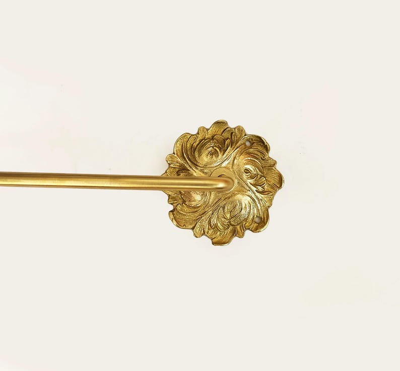 Op de afbeelding: Gouden metalen handdoekrek met een sierlijke, bloemvormige wandbevestiging.