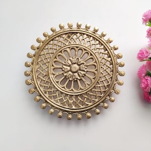 Puede incluir: Una bandeja redonda decorativa de metal dorado con un diseño intrincado que presenta un motivo floral central y un patrón tejido alrededor del borde.