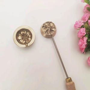 Op de afbeelding: Een set van twee messing bloemvormige mallen voor het maken van fondant- of gum paste-bloemen. De mal aan de linkerkant is een platte mal, terwijl de mal aan de rechterkant is bevestigd aan een houten handvat.