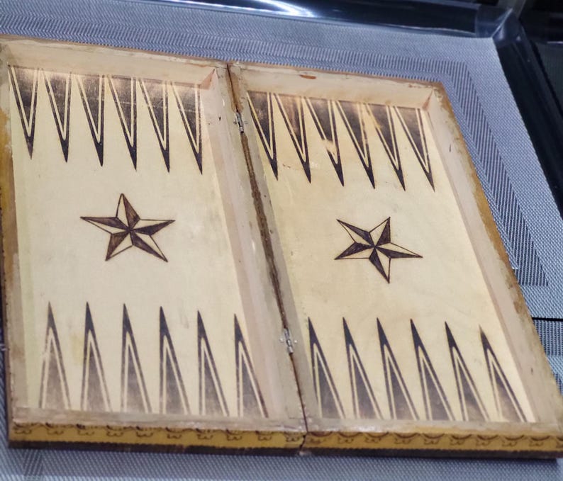 May include: A wooden backgammon board with a light brown finish. The board is closed and features two stars with a black outline on each side.