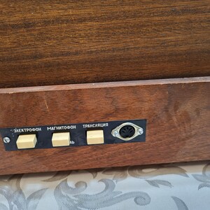 May include: Close-up of a wooden cabinet with a panel of buttons labeled "Электрофон", "Магнитофон", and "Трансляция".