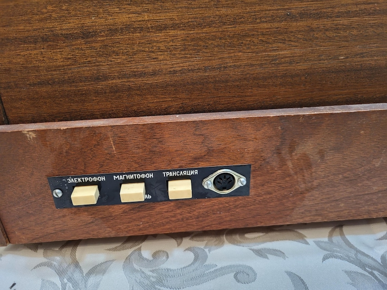 May include: Close-up of a wooden cabinet with a panel of buttons labeled "Электрофон", "Магнитофон", and "Трансляция".