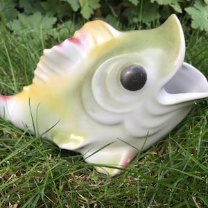 May include: A white ceramic fish figurine with green and yellow glaze. The fish has a large open mouth and a black eye.