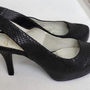 May include: Black snakeskin heeled slingback shoes with a pointed toe and a thin strap across the ankle. The shoes have a high heel and a platform sole.