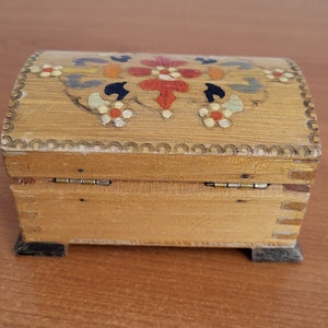 May include: A wooden box with a hinged lid. The lid is decorated with a colourful floral design painted in red, yellow, blue, and green. The box has a dark brown base.