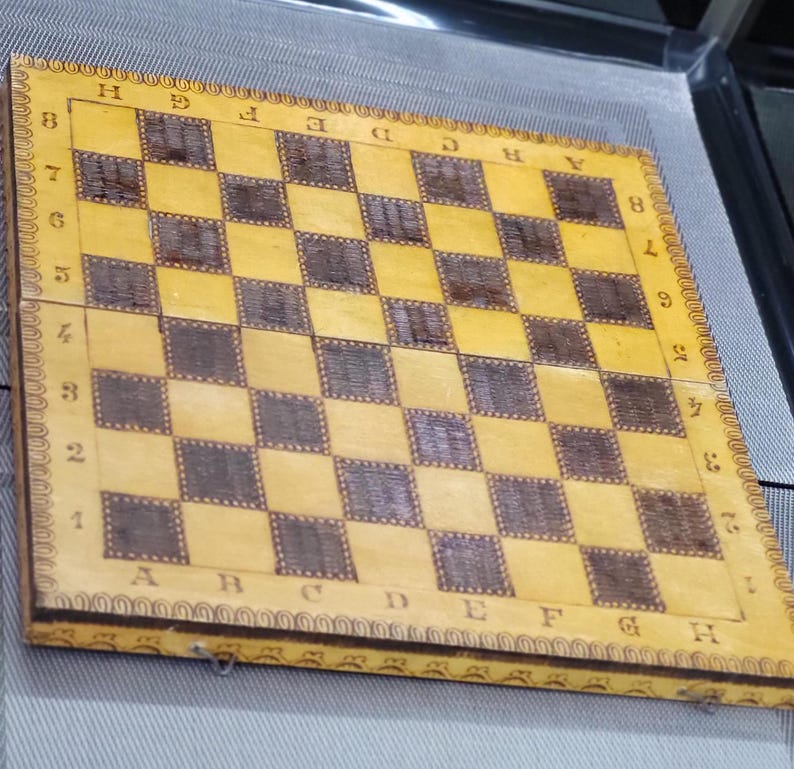 May include: A wooden chessboard with a yellow and brown checkered pattern. The board is labeled with letters A through H and numbers 1 through 8.