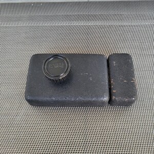 Puede incluir: Una funda de cámara negra con una tapa de lente. La funda es rectangular con una pequeña pieza rectangular adjunta en el lateral. La tapa de la lente es circular y tiene la palabra "FUJI" impresa.