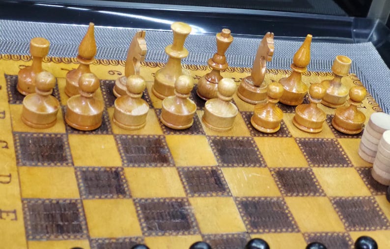 May include: A wooden chess set with light brown pieces on a brown and tan chessboard. The pieces include pawns, rooks, knights, bishops, a queen, and a king.