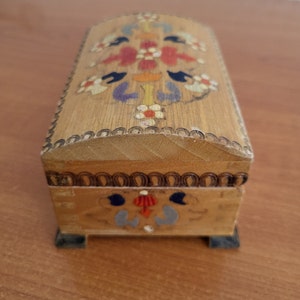 May include: A small wooden box with a hinged lid. The box is decorated with colourful painted flowers and a geometric pattern. The box has a dark brown trim around the edges.