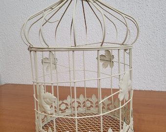 May include: A white metal birdcage with a decorative floral design. The cage has a round base and a domed top.