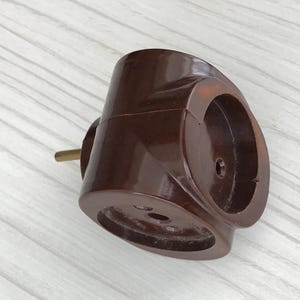 May include: A brown electrical adapter with three outlets. The adapter has a cylindrical body with a rounded shape and a brass-colored plug. The outlets are circular and recessed. The adapter is made of a glossy, dark brown material.