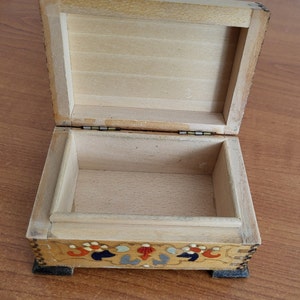 May include: A wooden box with a hinged lid and a painted floral design on the bottom. The box is open and the inside is empty.