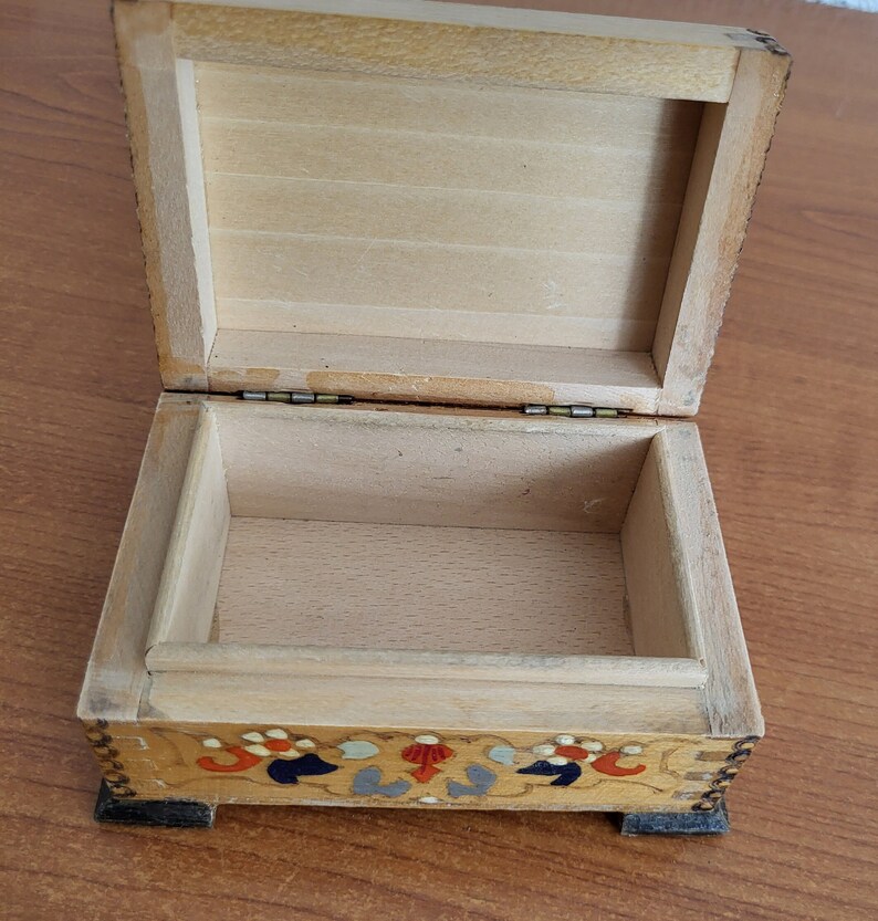 May include: A wooden box with a hinged lid and a painted floral design on the bottom. The box is open and the inside is empty.