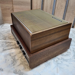 May include: A vintage wooden record player with a brown wood finish and a silver metal faceplate. The record player has a built-in speaker and a series of knobs on the front.