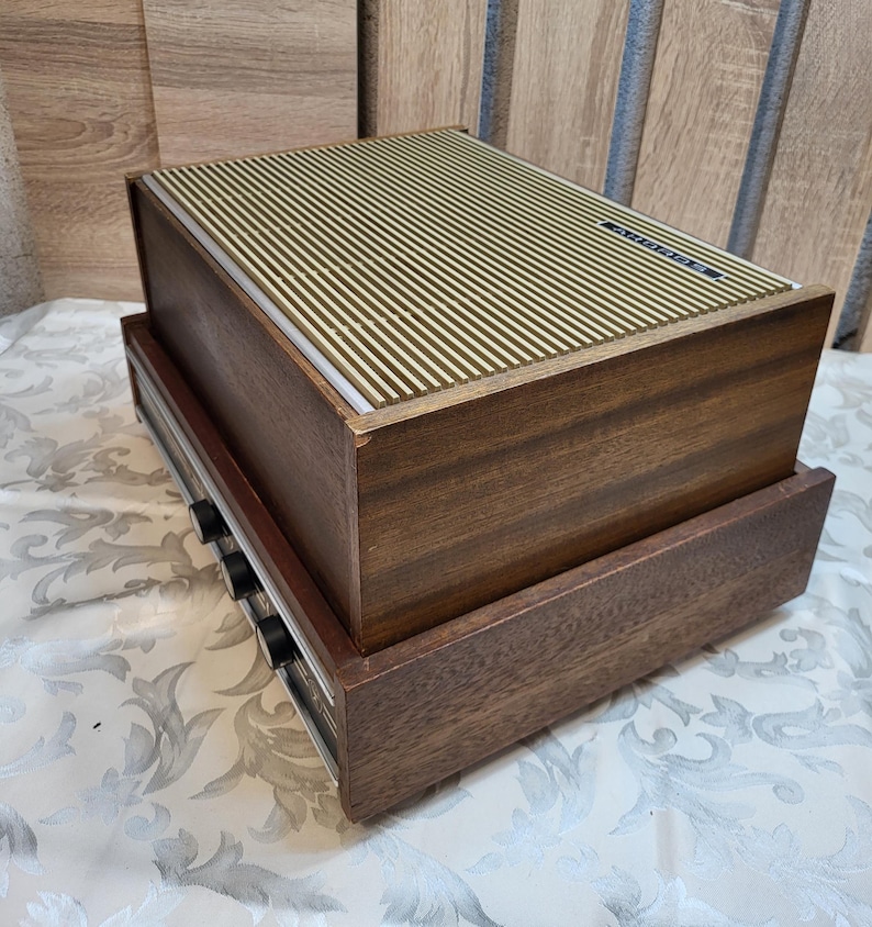 May include: A vintage wooden record player with a brown wood finish and a silver metal faceplate. The record player has a built-in speaker and a series of knobs on the front.