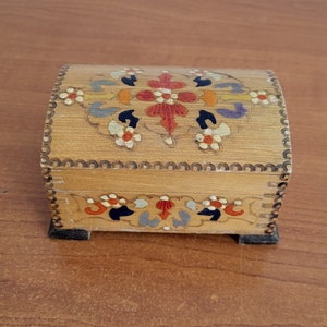 May include: A small wooden box with a hinged lid. The box is painted with a floral design in shades of red, orange, yellow, blue, and green. The box has a scalloped edge.