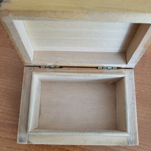 May include: An empty wooden box with a hinged lid. The box is made of light wood and has a natural finish. The inside of the box is lined with a smooth, white material.