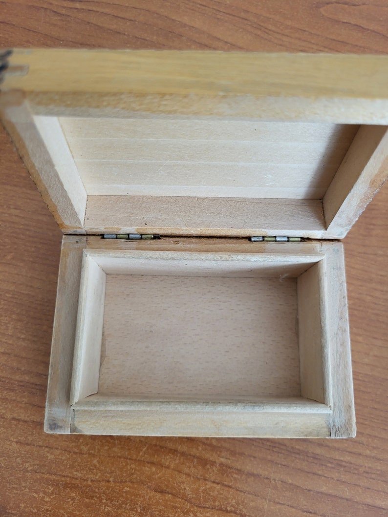 May include: An empty wooden box with a hinged lid. The box is made of light wood and has a natural finish. The inside of the box is lined with a smooth, white material.