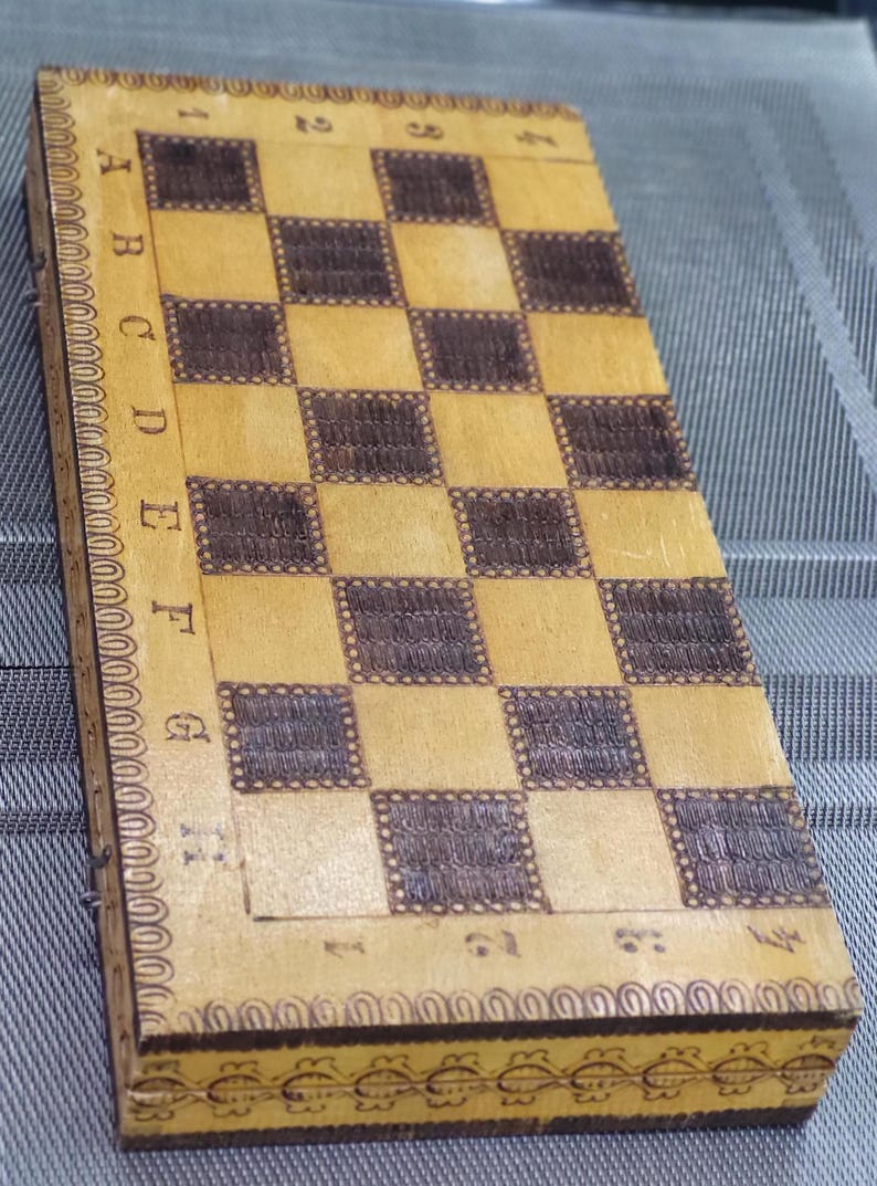 May include: A wooden chessboard with a brown and beige checkered pattern. The board is surrounded by a decorative border with a floral design.