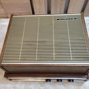 May include: A vintage wooden stereo receiver with a brown wood cabinet and a beige metal speaker grille. The receiver has a silver metal faceplate with three knobs and the text "AHOROS" printed on it.