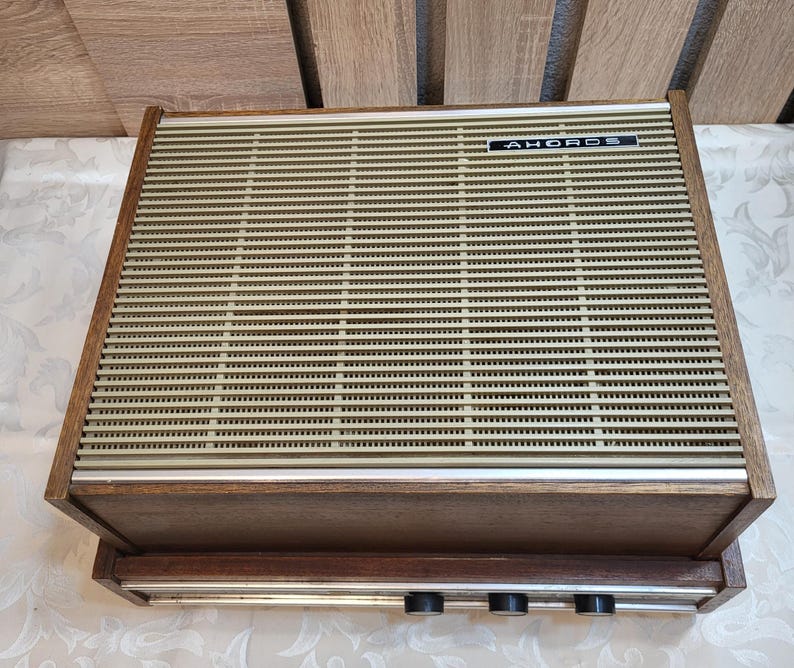 May include: A vintage wooden stereo receiver with a brown wood cabinet and a beige metal speaker grille. The receiver has a silver metal faceplate with three knobs and the text "AHOROS" printed on it.