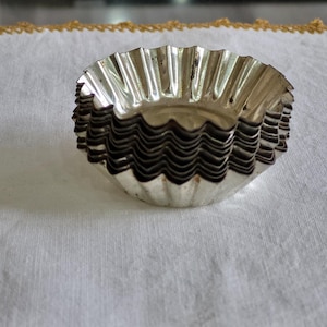 Puede incluir: Un conjunto de moldes para cupcakes de metal plateado con borde acanalado.