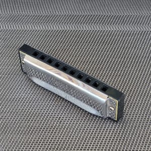 May include: A silver harmonica with black end caps and 10 holes. The harmonica is lying on a gray textured surface.