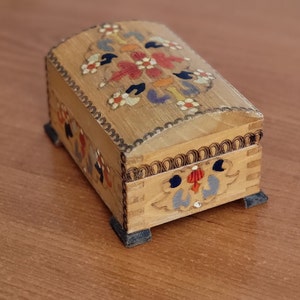 May include: A small wooden box with a hinged lid. The box is decorated with colourful floral patterns painted on the top and sides. The box has four small feet.