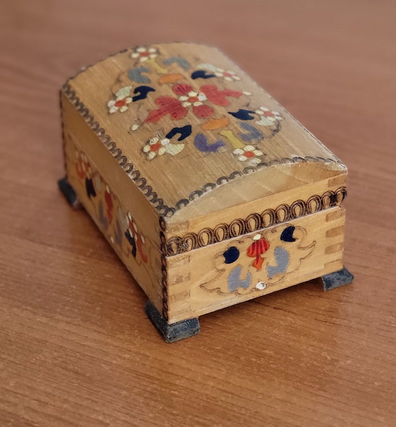 May include: A small wooden box with a hinged lid. The box is decorated with colourful floral patterns painted on the top and sides. The box has four small feet.