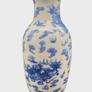 Puede incluir: Un jarrón de cerámica blanca con borde acampanado y cuerpo redondeado. El jarrón está decorado con motivos azules de nubes y criaturas míticas. El diseño se repite alrededor del jarrón, creando un patrón cohesivo. El jarrón tiene un acabado liso y brillante.