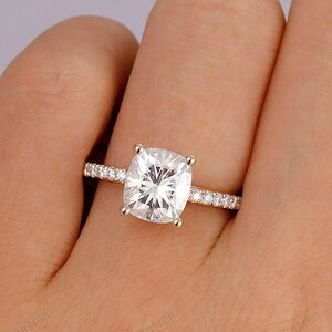 Peut inclure: Une bague de fiançailles en or avec une grosse pierre centrale carrée transparente et une bande de petites pierres transparentes.