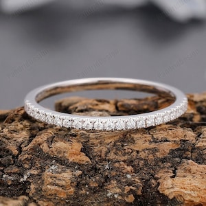 May include: A thin silver band with a row of small diamonds set in a pave setting. The band is on a piece of wood.