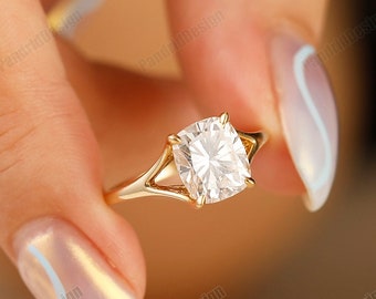 May include: A gold ring with a large, clear, square-shaped gemstone. The ring is held by a hand with light blue nail polish.