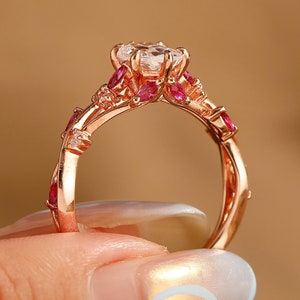 May include: A rose gold ring with a large, clear center stone and smaller pink stones around it.
