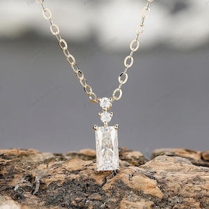 Op de afbeelding: Een gouden ketting met een rechthoekige hanger met een grote, heldere, gefacetteerde edelsteen. De hanger is versierd met twee kleinere, ronde edelstenen.