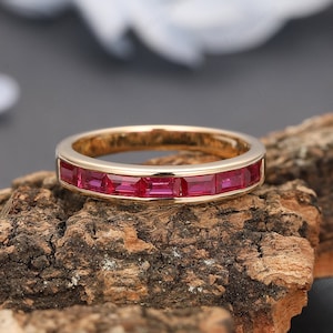 May include: A gold band ring with a row of red ruby stones set in a channel setting.