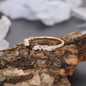 May include: A delicate gold band with a curved row of marquise and round diamonds. The ring is set on a wooden surface.